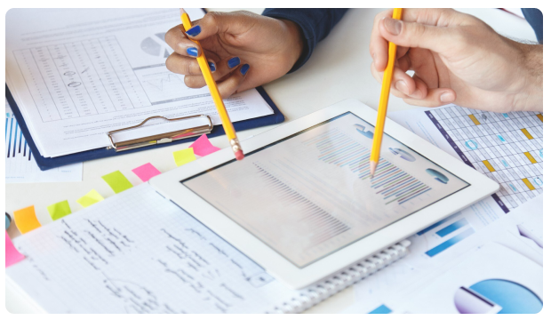 Two people pointing pencils at a tablet displaying financial charts